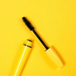 Open mascara with brush on vibrant yellow background, perfect for beauty and cosmetic themes.