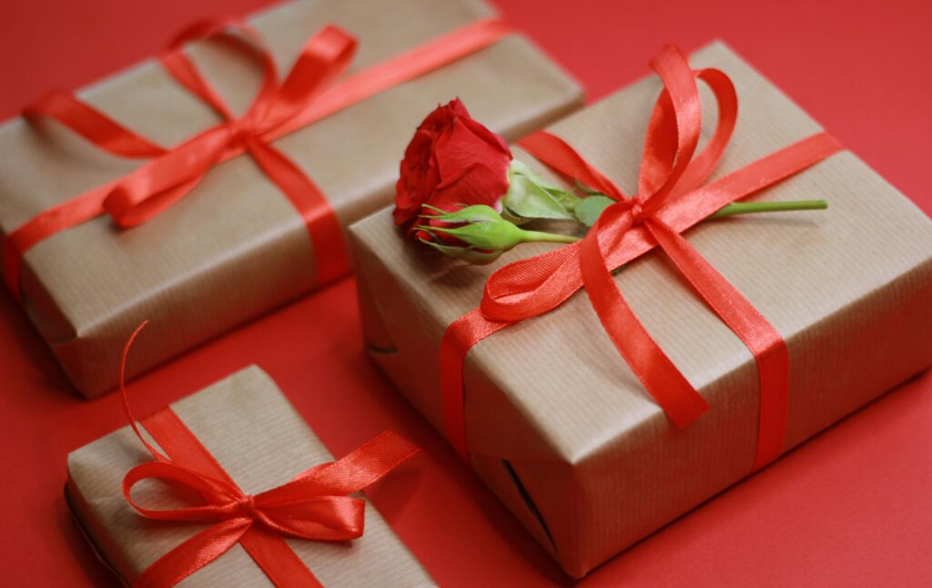 Elegant gift boxes tied with red ribbons and a rose on a red background.